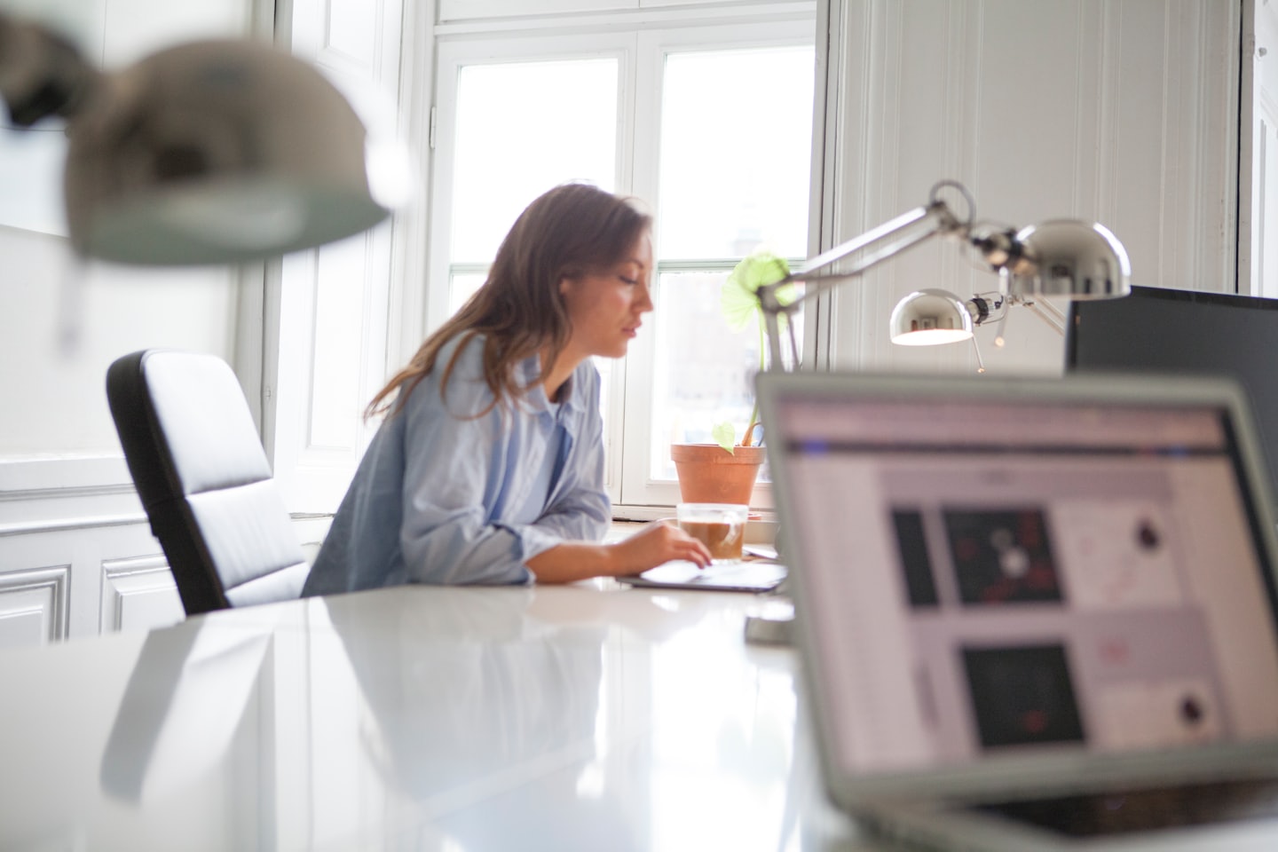 Woman works on laptop at a modern white desk.