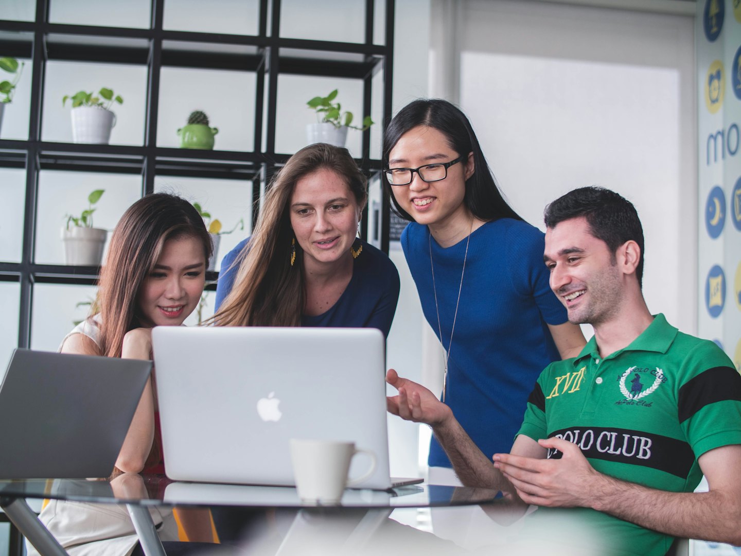 Four diverse professionals collaborate around a laptop in a modern office.